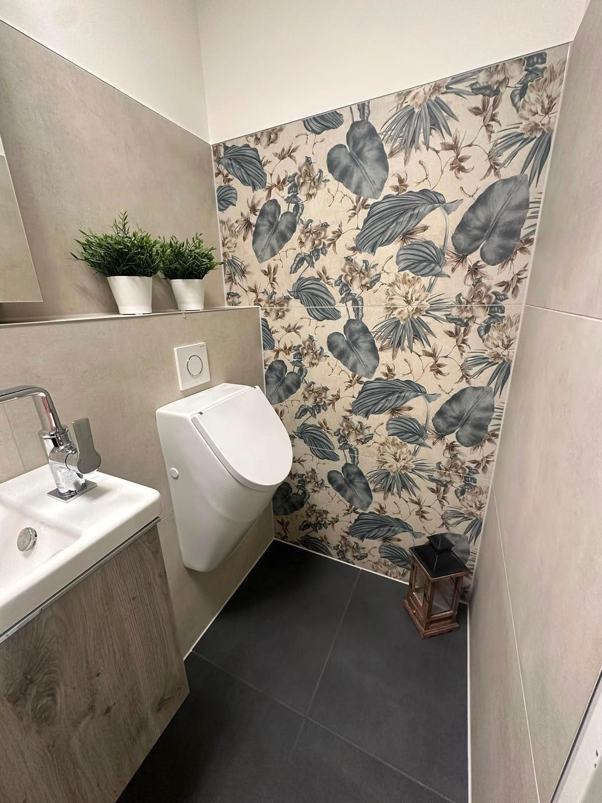 Gäste-WC mit floral gemusterten Wandfliesen, Urinal, kleinem Waschbecken und Boden in Betonoptik