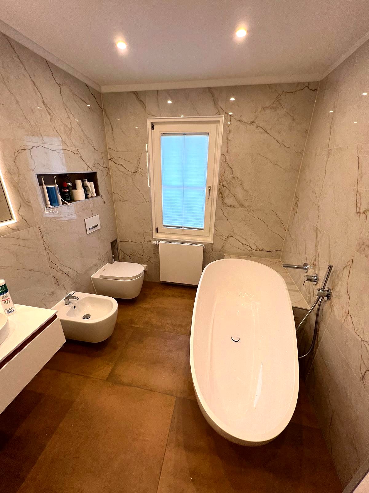 Bad in Marmoroptik mit freistehender Wanne, Bidet und bodentiefem Fenster