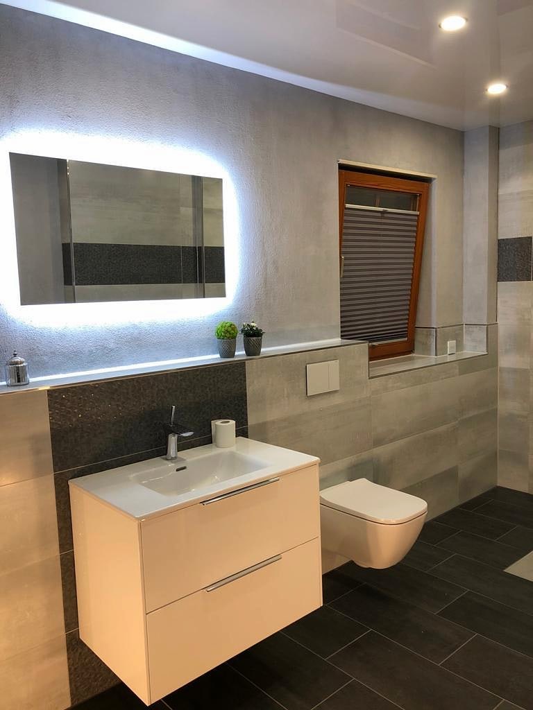 Badezimmer mit Betonoptik-Fliesen, umlaufendem Mosaikband und hinterleuchtetem Spiegel