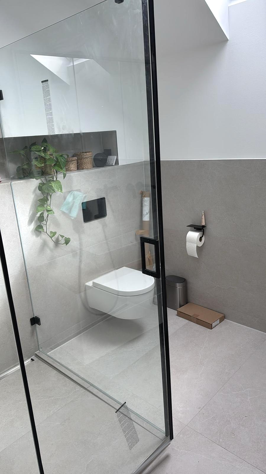 Bodengleiche Dusche mit Glaswand neben Wand-WC in einem hellen Bad
