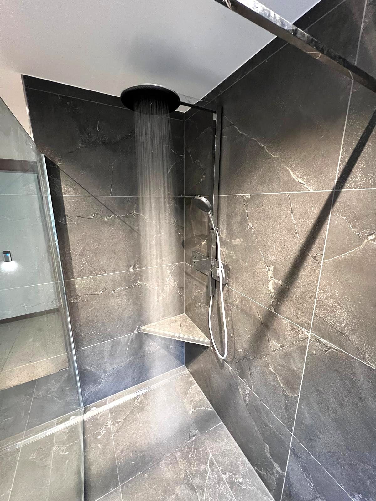 Dusche mit anthrazitfarbenen Marmoroptik-Großformatfliesen und laufender Regendusche