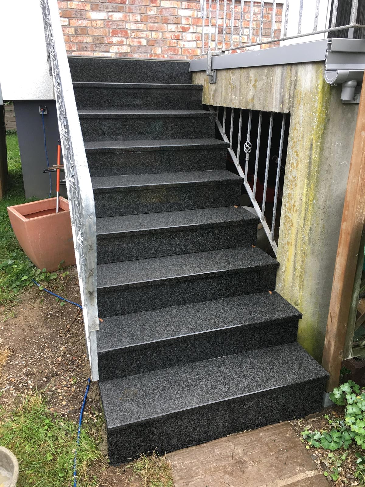 Außentreppe mit dunklen Granitstufen und Metallgeländer an einer Hauswand