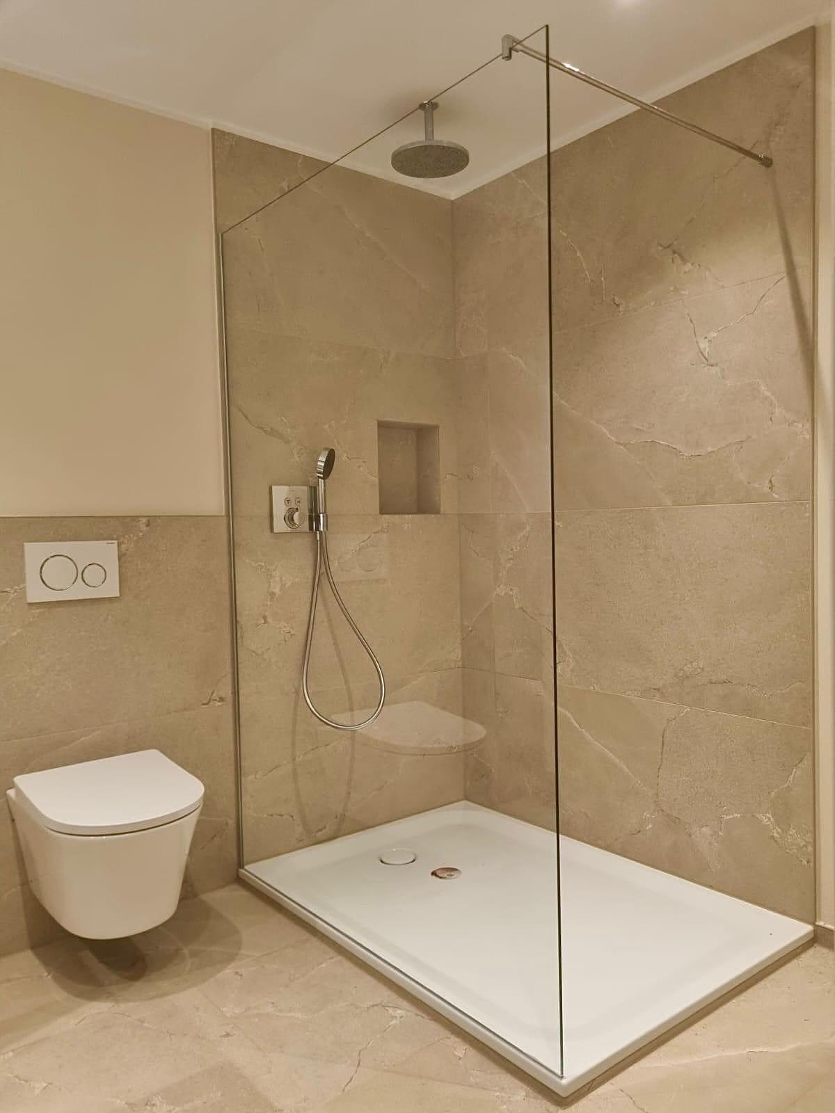 Fertiges Bad mit beigen Marmoroptik-Großformatfliesen, rahmenloser Glaswand, Regenbrause und Wand-WC